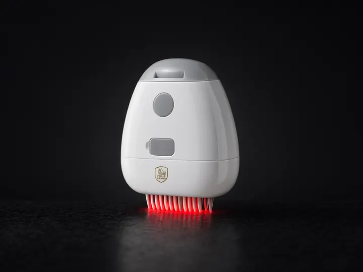 White powered scalp applicator with a small YOUR BRAND shield, red light glowing between its comb teeth, on black